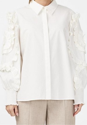 Chemise blanche avec manches à volants, devant à boutons et col. La texture du tissu semble lisse avec une coupe ample. Design arrière uni.