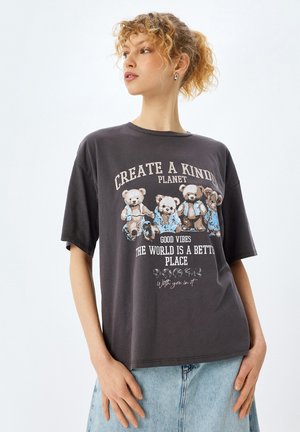 T-shirt oversize gris à manches courtes, présentant un graphique d'ours et du texte. Texture douce, design décontracté et slogan illustré sur le devant.