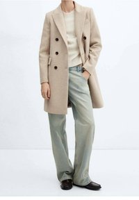 Beige dobbeltradet frakke med sorte knapper, parret med lysegrønne brede bukser og mørke loafers. Blød tekstur, skræddersyet design.