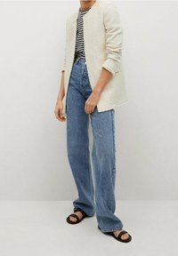 Witte, gestructureerde blazer over een gestreepte zwart-wit shirt, gecombineerd met hoge blauwe jeans en zwarte sandalen. Casual outfit ontwerp.