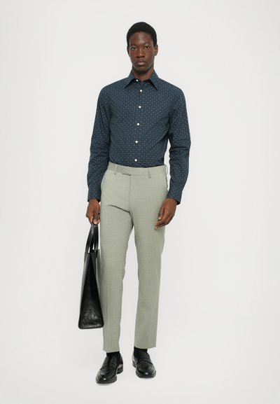 Koszula w granatowy wzór, jasnoszare spodnie, czarne skórzane buty i czarna torba typu tote. Slim fit, gładka tkanina, prosty kołnierzyk.