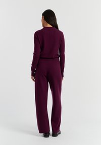 Lila Strickpullover mit geripptem Kragen, kombiniert mit passenden weiten Hosen. Glatte Textur, tailliert und durchgängig in einer einheitlichen Farbe.