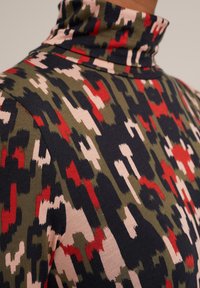 Svetr s vysokým límcem s vícebarevným abstraktním vzorem v zelené, červené, černé a krémové barvě. Měkká tkanina s přiléhavým střihem.