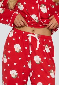 Roter Baumwoll-Schlafanzug mit weißen Sternmustern und illustrierten Weihnachtsmann-Gesichtern, ergänzt durch Leoparden-Akzente. Elastischer Taillenbund mit Zugband.