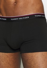 Svart bomulls boxertights med en merkevare-elastisk midjebånd som har "TOMMY HILFIGER" og røde og hvite detaljer. Glatt, tettsittende design.