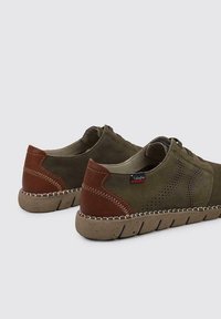 Zapatos verde oliva con acentos de cuero marrón, diseño perforado en los lados y una suela gruesa moteada. Cierre con cordones y detalles de costura.