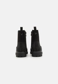 Bottines noires avec des panneaux en daim et en tissu texturé, fermetures éclair à l'arrière et semelles en caoutchouc avec grip, conçues pour la durabilité et le confort.
