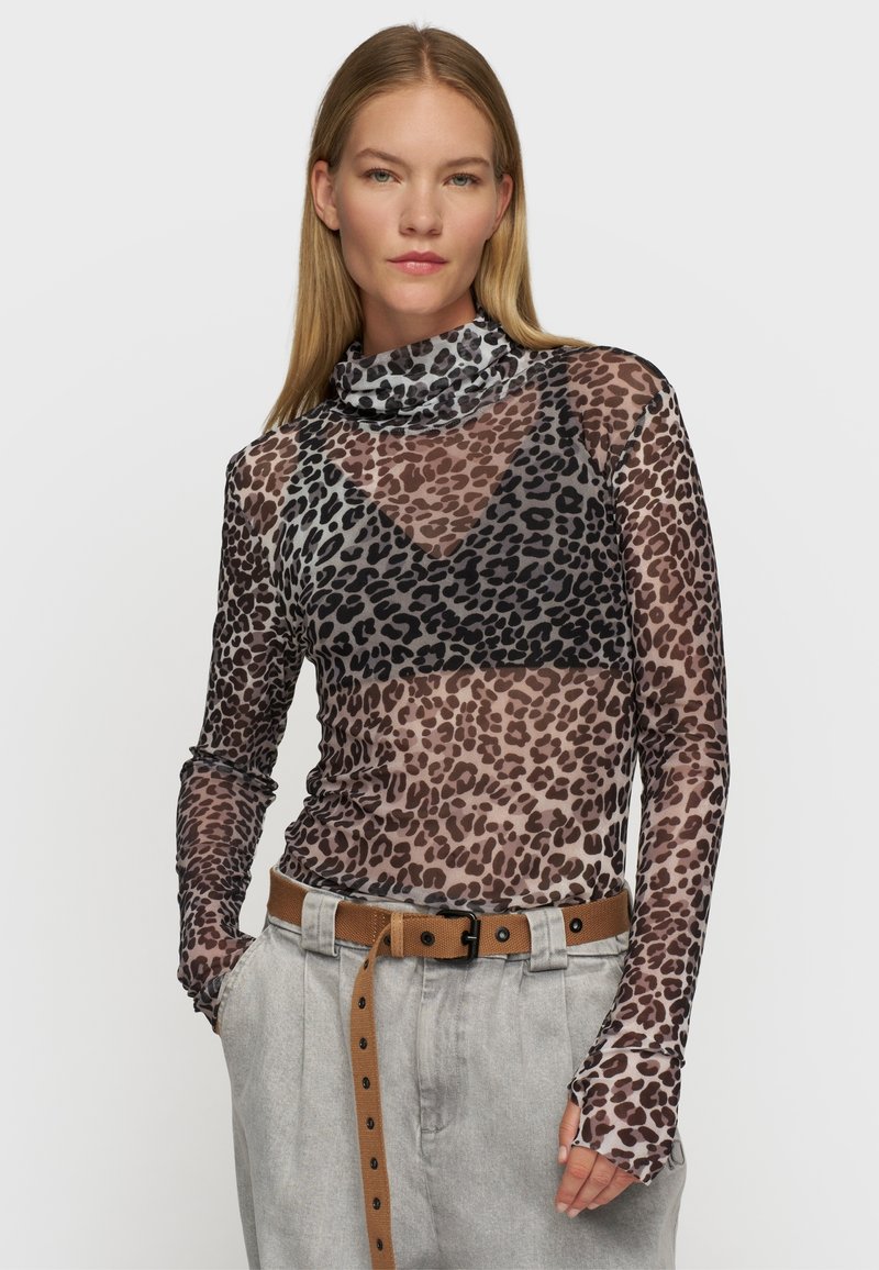 Durchsichtige Bluse mit langen Ärmeln im Leopardenmuster in Brauntönen und Schwarz. Mit einem hohen Kragen und figurbetontem Schnitt, kombiniert mit hochtaillierten, hellgrauen Hosen.