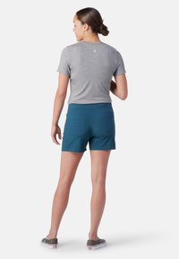 Graues Kurzarmshirt mit einem dezenten Logo auf dem Rücken, kombiniert mit türkisfarbenen Shorts, die eine glatte Textur und zwei Gesäßtaschen aufweisen.