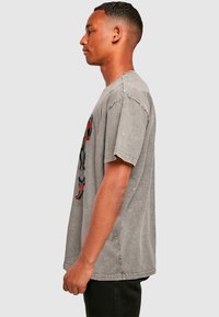 Gray oversized t-shirt made of cotton. Features short sleeves and a graphic print on the front depicting figures in red and black.