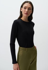 Zwarte ribbel trui met lange mouwen en een ronde hals, gecombineerd met olijfgroene satijnen broek met zijzakken en een gladde textuur.