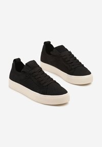 Baskets noires avec une tige en maille, présentant un design texturé, des lacets plats et une semelle en caoutchouc blanc. Style minimaliste avec des accents subtils.
