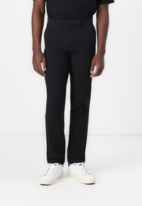 Black tailored trousers with a button closure, belt loops, and a slim fit design. Paired with white sneakers for a casual look.