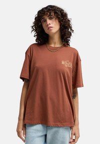 Rostfarbiges, locker sitzendes T-Shirt aus Baumwolle, mit einem kleinen gestickten Blumenmuster auf der linken Brust und entspannten kurzen Ärmeln.