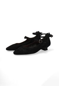 Een paar zwarte suède schoenen met lage hakken, enkelbandjes en gespen, met spitse neuzen, tentoongesteld tegen een witte achtergrond.