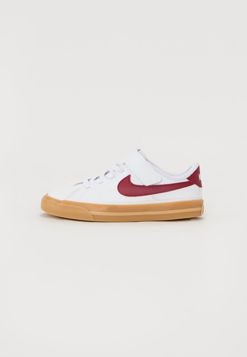 Sneaker blanc basse avec swoosh rouge Nike, semelle en gomme, lacets et une bride velcro sur la languette, présenté sur un fond uni.