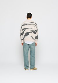 Túlméretezett krémszínű pulóver absztrakt szénszürke mintával, bolyhos anyagból készült, kék farmernadrág fölött viselve, világos színű cipőkkel.