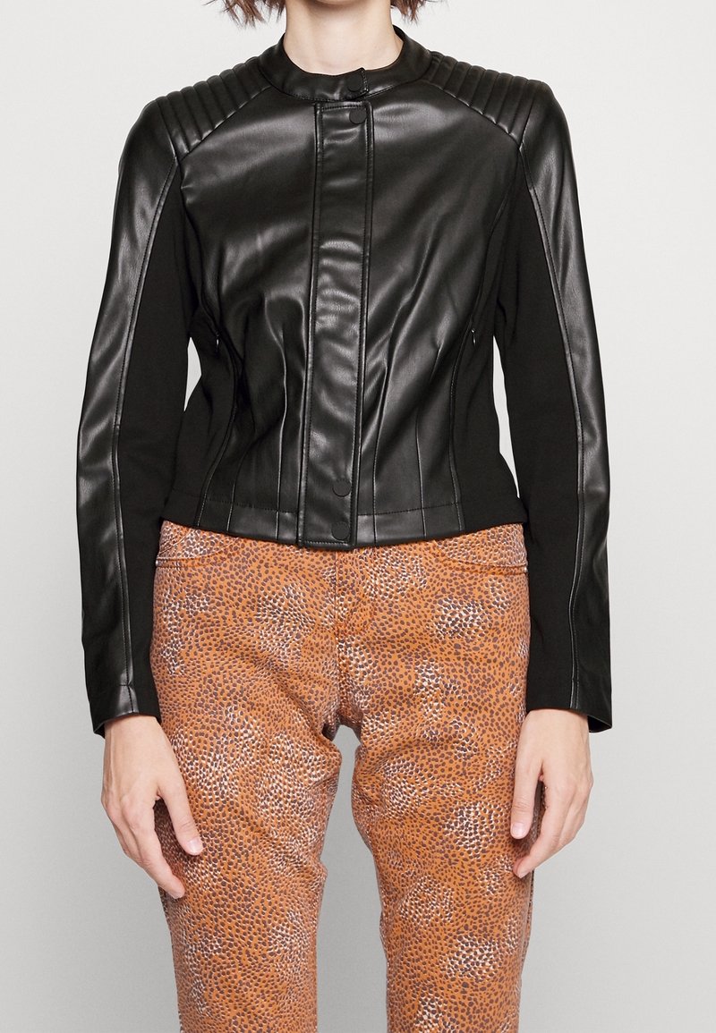 Schwarze Lederjacke mit gerippten Schulterakzenten, schmaler Passform und hohem Kragen, kombiniert mit gemusterten braunen Hosen.