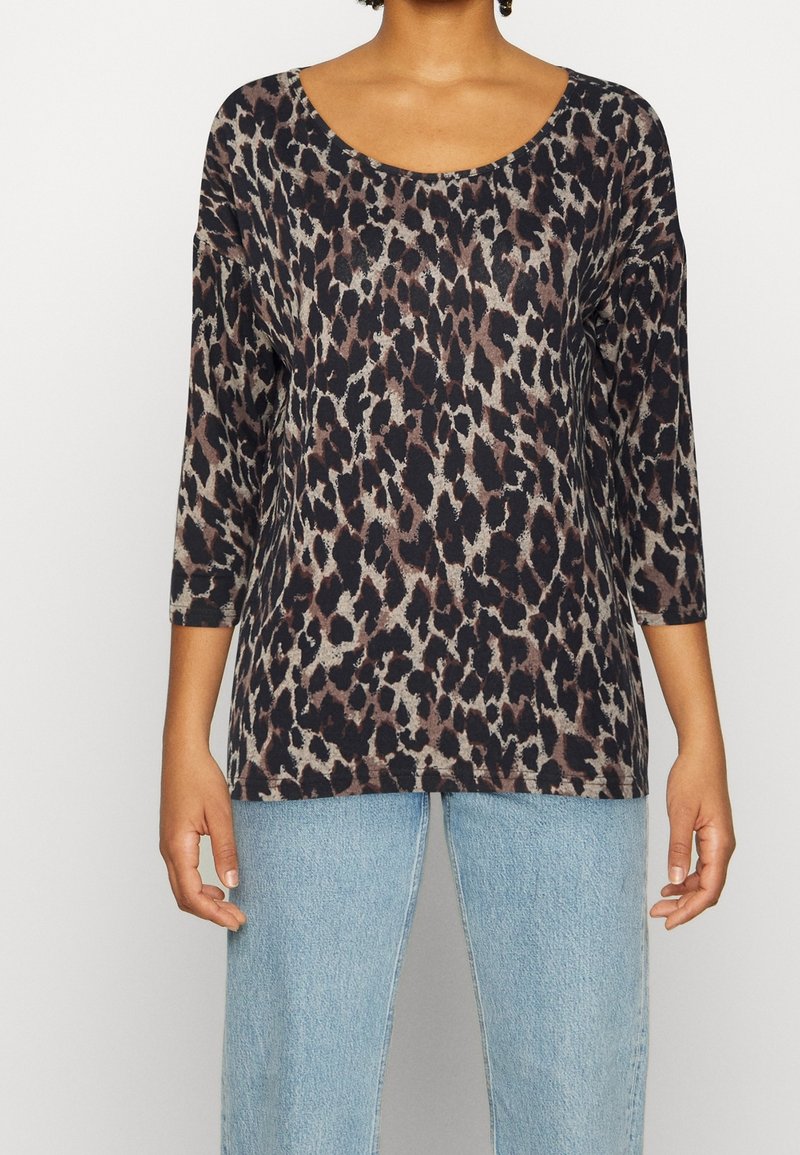 Leopardskinn mönstrad långärmad topp i mörka toner, med rundad halsringning och avslappnad passform. Kombineras med ljusblåjeans för en avslappnad look.
