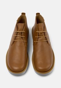 Scarpe in pelle marrone con una texture liscia, caratterizzate da un design a caviglia bassa, punta rotonda e dettagli di lacci minimi. Suola sottile e a contrasto.
