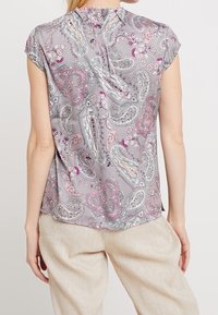 Blouse en satin à motif cachemire gris, dotée de manches courtes, d'un col rond et d'une ouverture en forme de goutte dans le dos. Le design comprend des motifs cachemire multicolores.