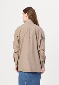 Beige, oversize, gombos ing, gallérral, hosszú ujjakkal és mandzsettagombokkal. Egyszerű dizájn, könnyű anyagból készült.
