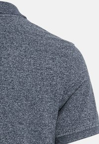 Koszulka polo z krótkim rękawem z teksturowanej ciemnoszarej tkaniny. Posiada klasyczny kołnierzyk i staranne wykończenia krawędzi.