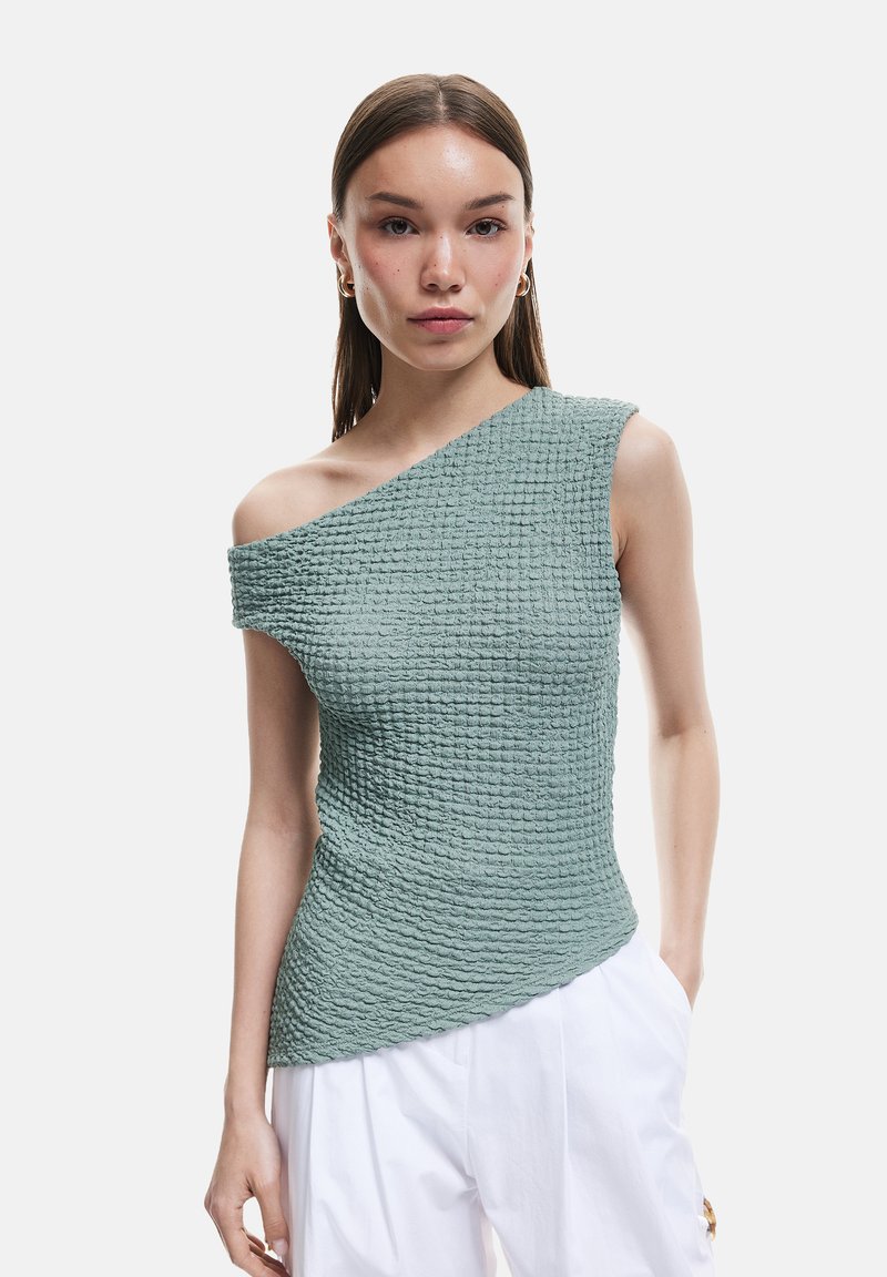 Haut asymétrique à une épaule en tissu texturé vert sauge, présentant une silhouette ajustée et un ourlet légèrement ondulé. Design minimaliste.