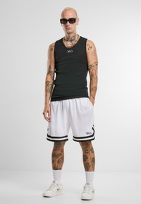 Juodas marškinėliai be rankovių, balti krepšinio šortai su juodomis juostelėmis ir balti sportbačiai. Modelis turi šviesių plaukų ir tatuiruotes.