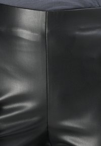 Schwarze Kunstlederhosen mit glatter Textur und schickem Finish. Eine Nahaufnahme zeigt die Nähte und leichte Falten auf der Stoffoberfläche.