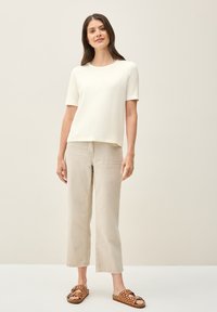 Cremefarvet t-shirt med korte ærmer, kombineret med lysebeige brede bukser og brune sandaler med prikker. Enkel, afslappet pasform.