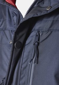 Marineblaue Jacke aus strukturiertem Material, mit einem Reißverschluss, elastischem Kordelzug, Druckknopf und kontrastierendem roten Innenfutter.