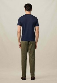 Camiseta de algodón azul marino con mangas cortas y cuello redondo, combinada con pantalones verde oliva, vista desde atrás.