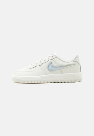 Basket basse blanche Nike avec logo swoosh bleu clair, bout perforé et semelle en caoutchouc sur fond clair uni.