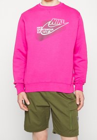 Pink crewneck sweatshirt with Nike logo and text, paired with green cargo shorts featuring side pockets and a zipper detail.