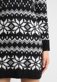 Maglione lavorato a maglia in bianco e nero con un motivo a fiocchi di neve, caratterizzato da vari designs geometrici, polsini a coste e una finitura testurizzata.