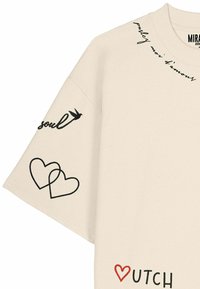 Camicia beige a maniche corte con testo nero e grafiche a forma di cuore su colletto, manica e parte inferiore frontale, incluso "soul" e cuore rosso vicino a "UTCH."
