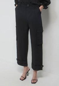 Schwarze Cargo-Hosen mit hoher Taille, hochgerollten Bündchen und mehreren Taschen. Hergestellt aus glattem Stoff mit Knopfverschluss und taillierter Passform.
