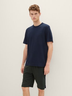 Dunkelblaue Baumwoll-T-Shirt mit kurzen Ärmeln, Rundhalsauschnitt und dezenten Nähten, kombiniert mit dunkelgrünen Shorts mit strukturiertem Finish.