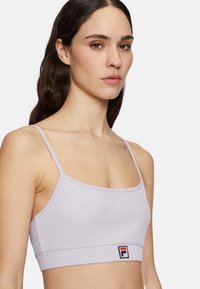 Lila ribbad sportbh med tunna band, med en logotyp i rött, vitt och blått på en solid rem. Slät yta och figurnära design.