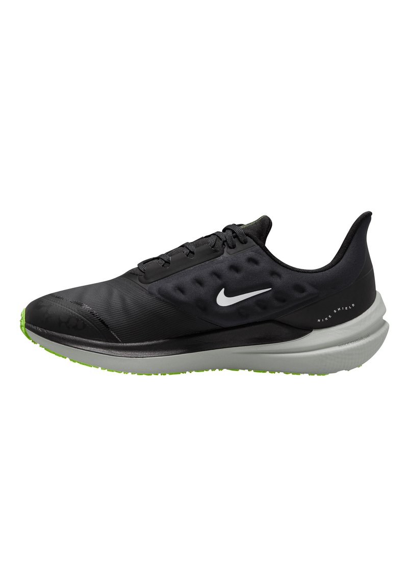 Zapatilla deportiva negra con parte superior suave, sistema de cordones y suela negra texturizada. Presenta una suela verde y el logo de Nike reflectante.