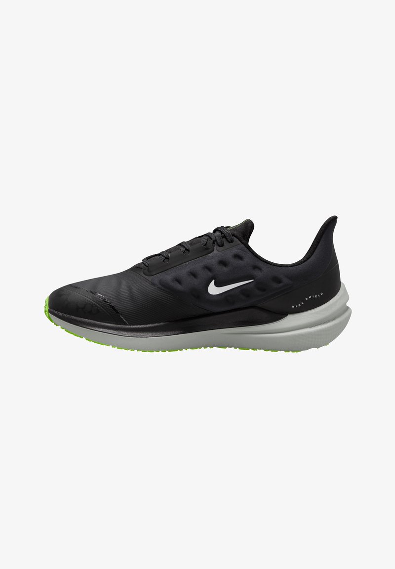 Baskets de sport noires avec une tige lisse, un système de laçage et une semelle noire texturée. Comprend une semelle extérieure verte et un logo Nike réfléchissant.