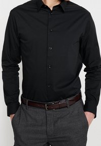 Zwarte languithemd met knoopsluiting, slim fit, gladde stof; gecombineerd met grijze, gestructureerde broek en een bruine leren riem.