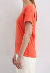 Lys orange kortærmet T-shirt med en afslappet pasform, rund halsudskæring og oprullede ærmer. Letvægtsstof med subtile teksturdetaljer.