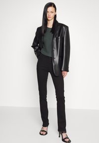 Black faux leather blazer over a dark green top, paired with black skinny jeans and black heeled sandals. Smooth texture and tailored fit.