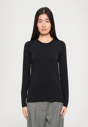 Camisola preta de mangas longas feita de um tecido macio, com decote redondo e um corte justo, combinada com calças cinzas com padrão.