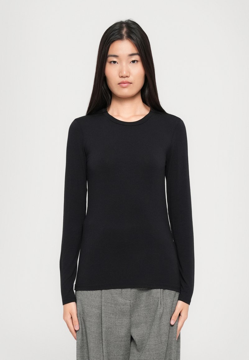 Long-sleeve black top made from soft fabric, featuring a round neckline and a slim fit, paired with patterned gray trousers.