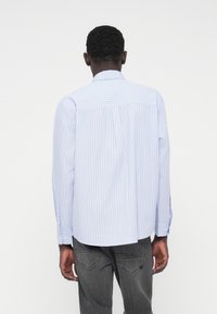 Ανοιχτό μπλε ριγέ πουκάμισο με μακριά μανίκια, γιακά με κουμπιά και στρογγυλεμένο στρίφωμα. Κατασκευασμένο από απαλό ύφασμα, με άνετη εφαρμογή και κουμπιά στα μανίκια.