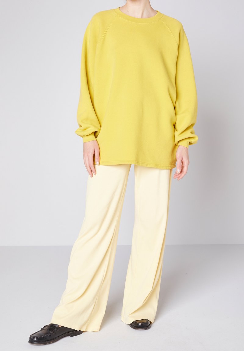 Gul oversized tröja med ribbade muddar som kombineras med ljust gula vida byxor. Outfiten har en mjuk, texturerad tyg och en avslappnad passform.