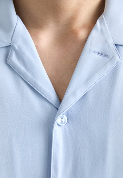 Lichtblauw overhemdd shirt met een gladde textuur, een notch-kraag en een enkele knoopsluiting. Beschikt over subtiele stikseldetails.